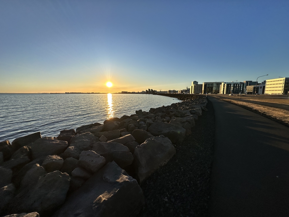 Sunset over the sea with rocks and a city skyline in the distance.