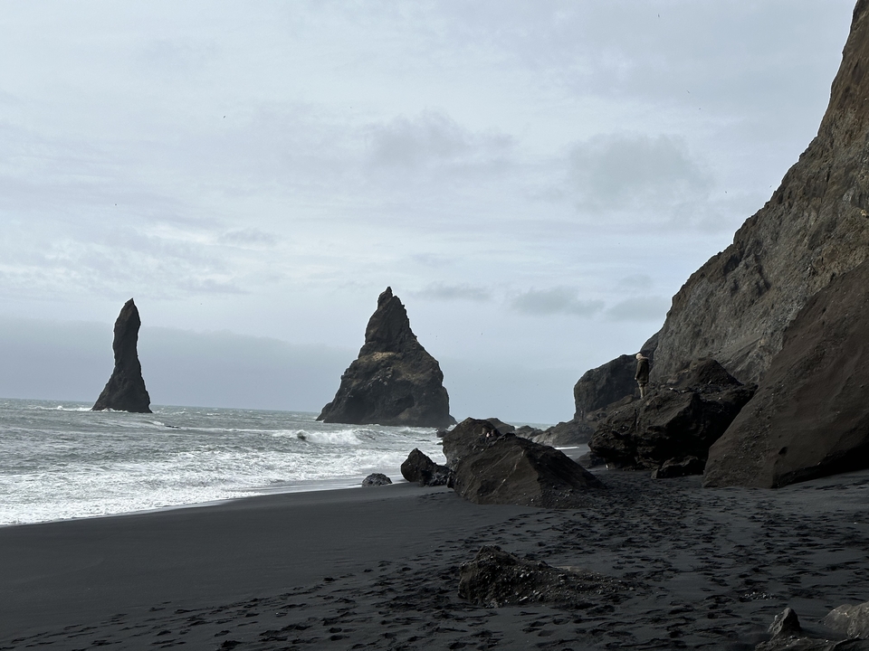 A rugged coastline with sea stacks and black sandy shore.