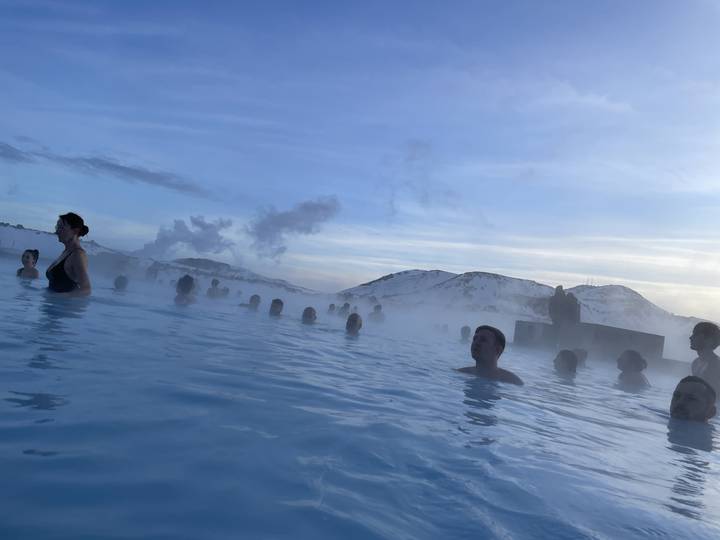People relaxing in a thermal pool with a mountainous background.