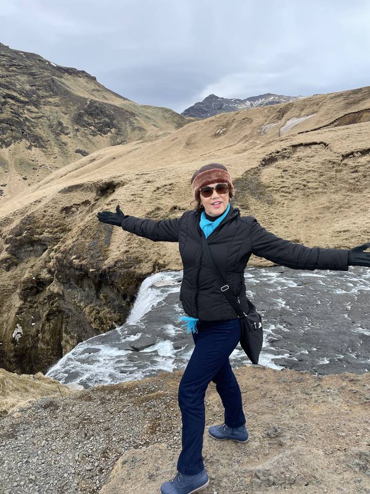 Person posing by a waterfall in a natural setting.