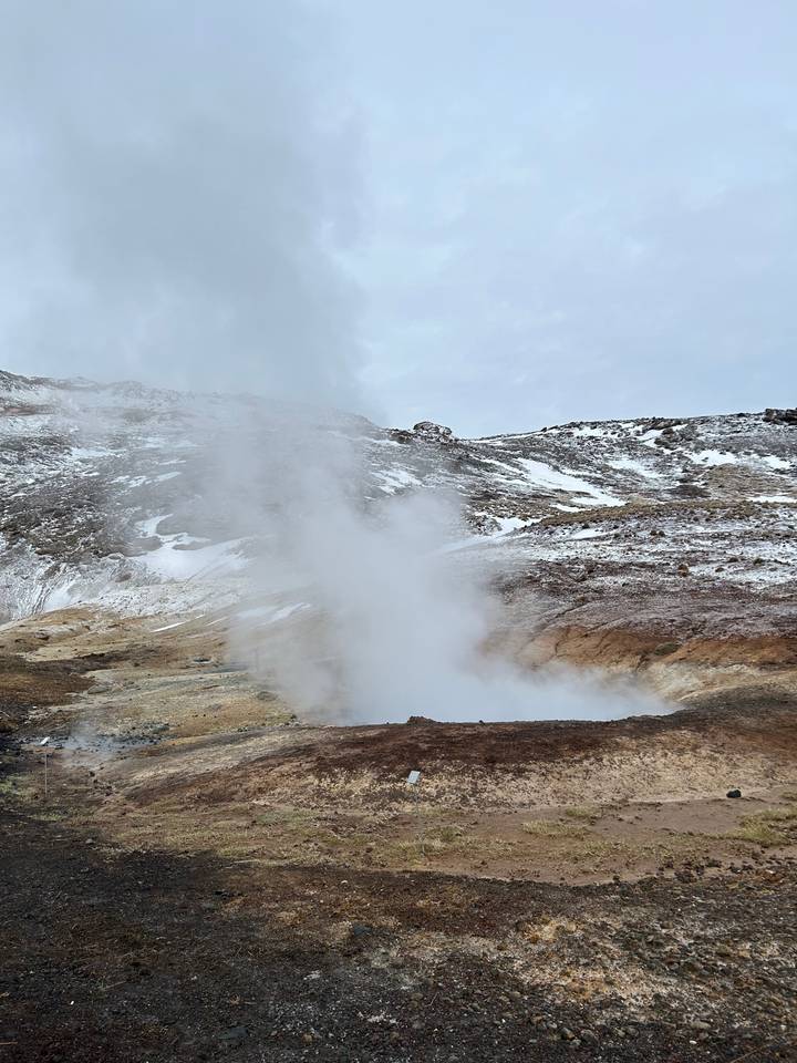 Steaming landscape with geothermal activity amidst snowy terrain.