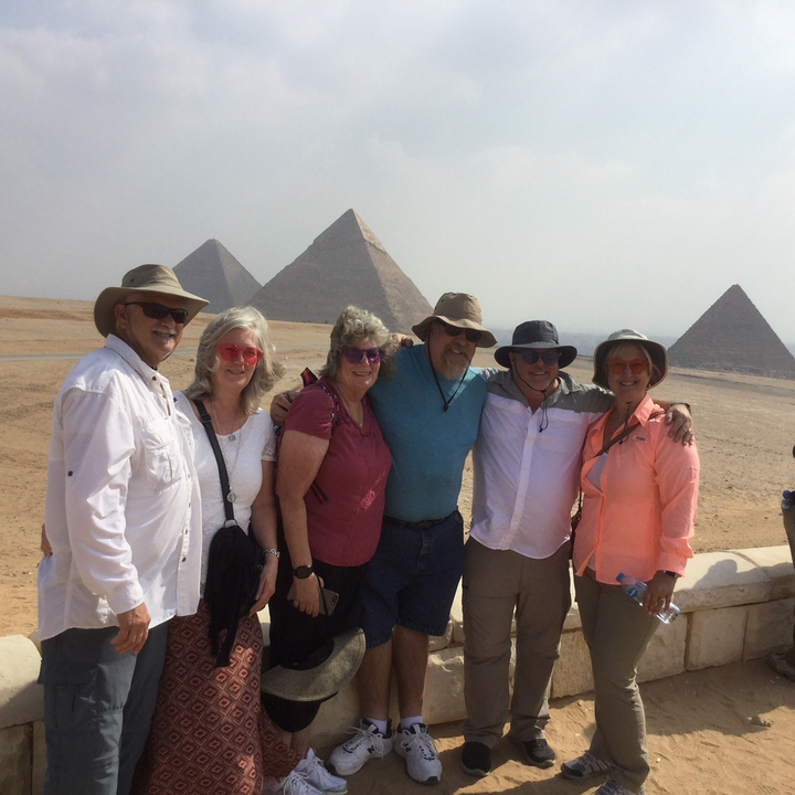 Group of people posing in front of pyramids with desert background.