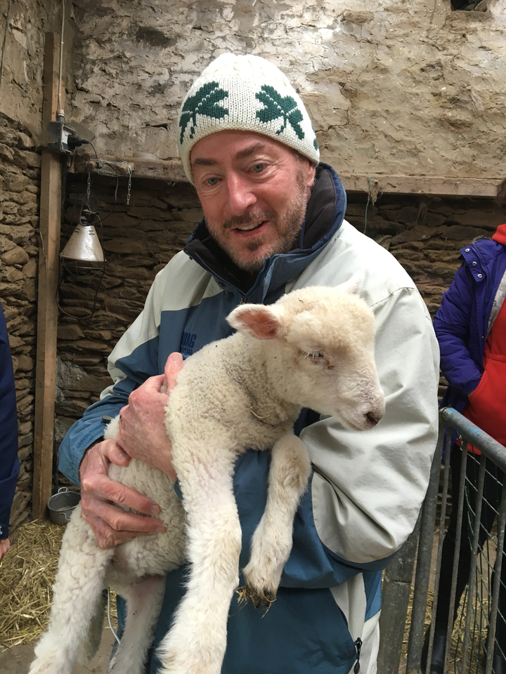 Homme berçant joyeusement un agneau dans une étable