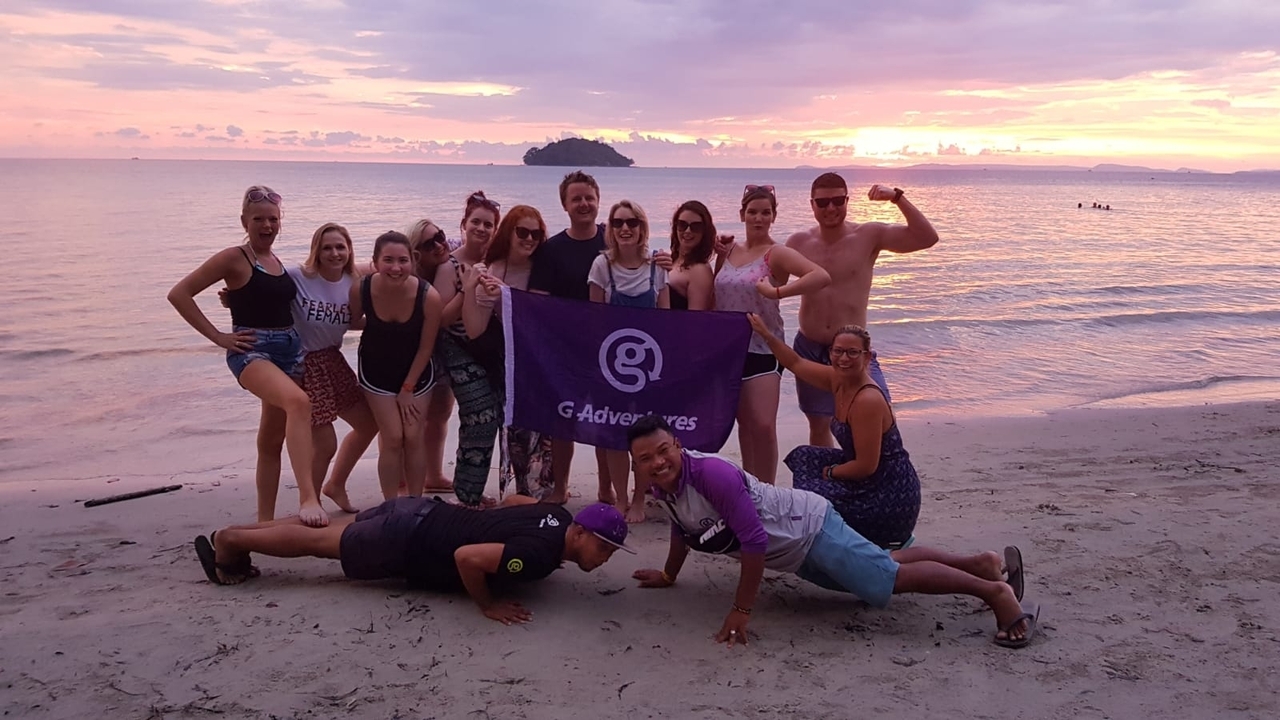Groupe tenant une bannière de voyage sur la plage pendant le coucher du soleil.