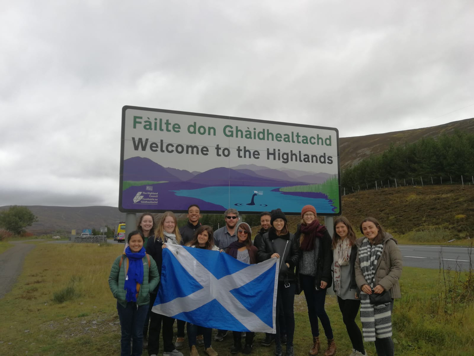Group of people with a Scotland flag at a highlands sign.