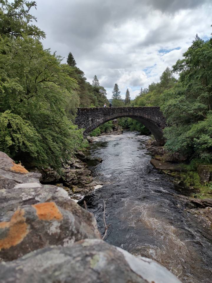 Stone bridge over a rushing river surrounded by trees.