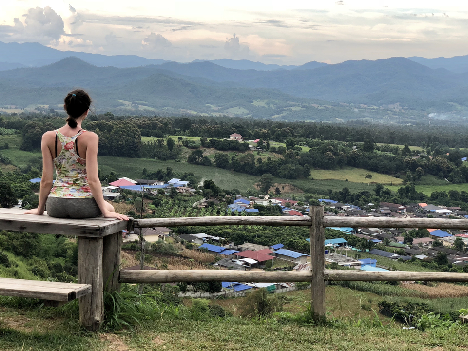 A person sitting on a fence overlooking a village and hills.