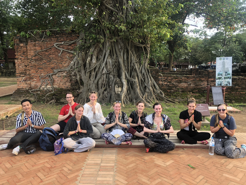 People sitting together in front of a tree with a carved face.