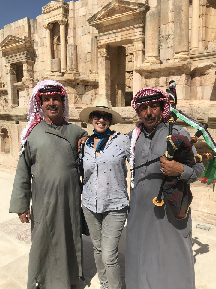 Femme souriante avec deux hommes en tenue traditionnelle tenant des cornemuses.