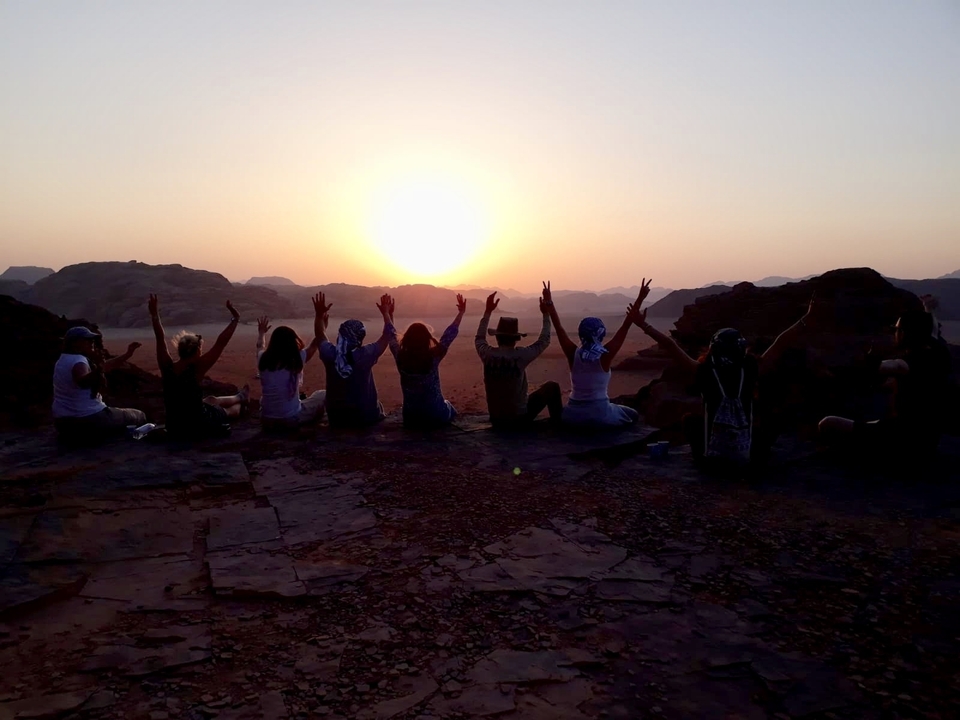 Silhouettes de personnes aux bras levés regardant un coucher de soleil sur le désert.