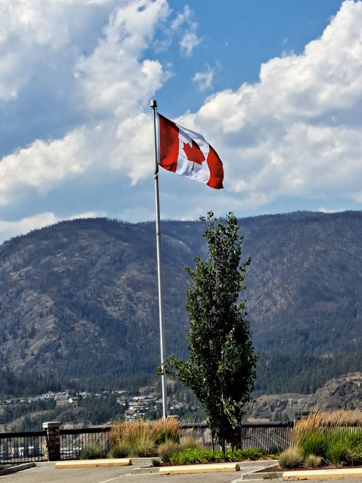 Canadian flag on a pole with distant mountains.