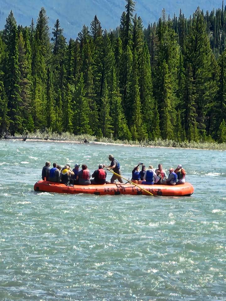 People rafting on a river surrounded by forested hills.