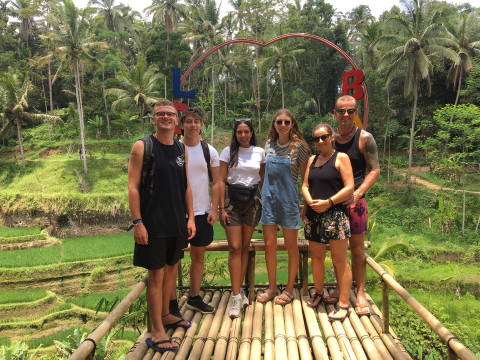 Group posing in front of rice terraces with tropical vegetation.