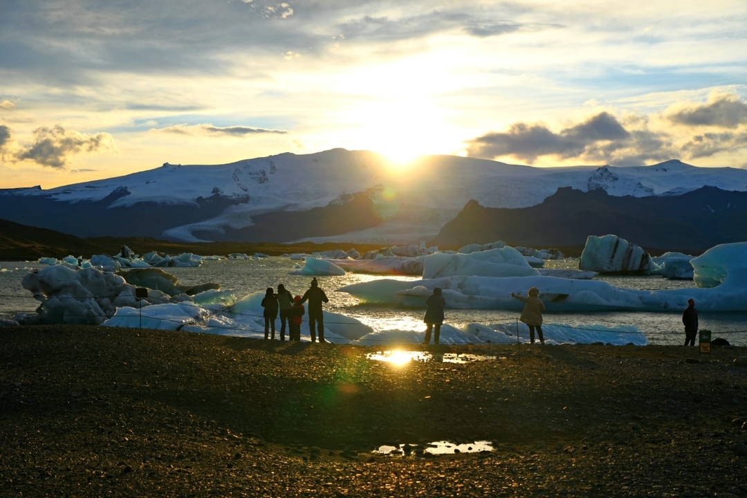 People observing floating icebergs under a setting sun.