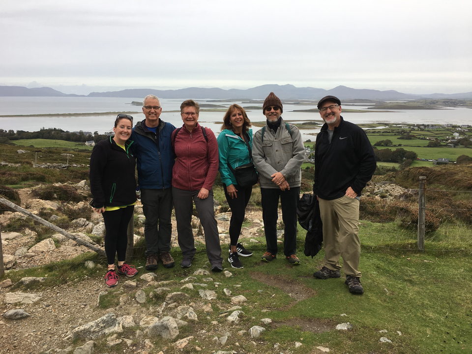 Small group of people posing with a scenic lake and hills in the background.