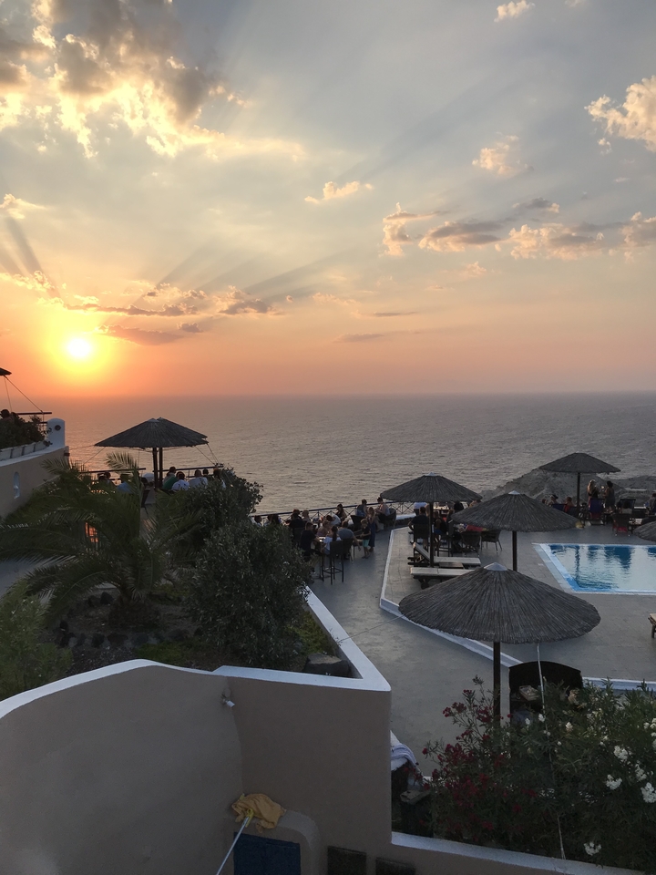 Sunset over a cliffside with people dining at a terrace.