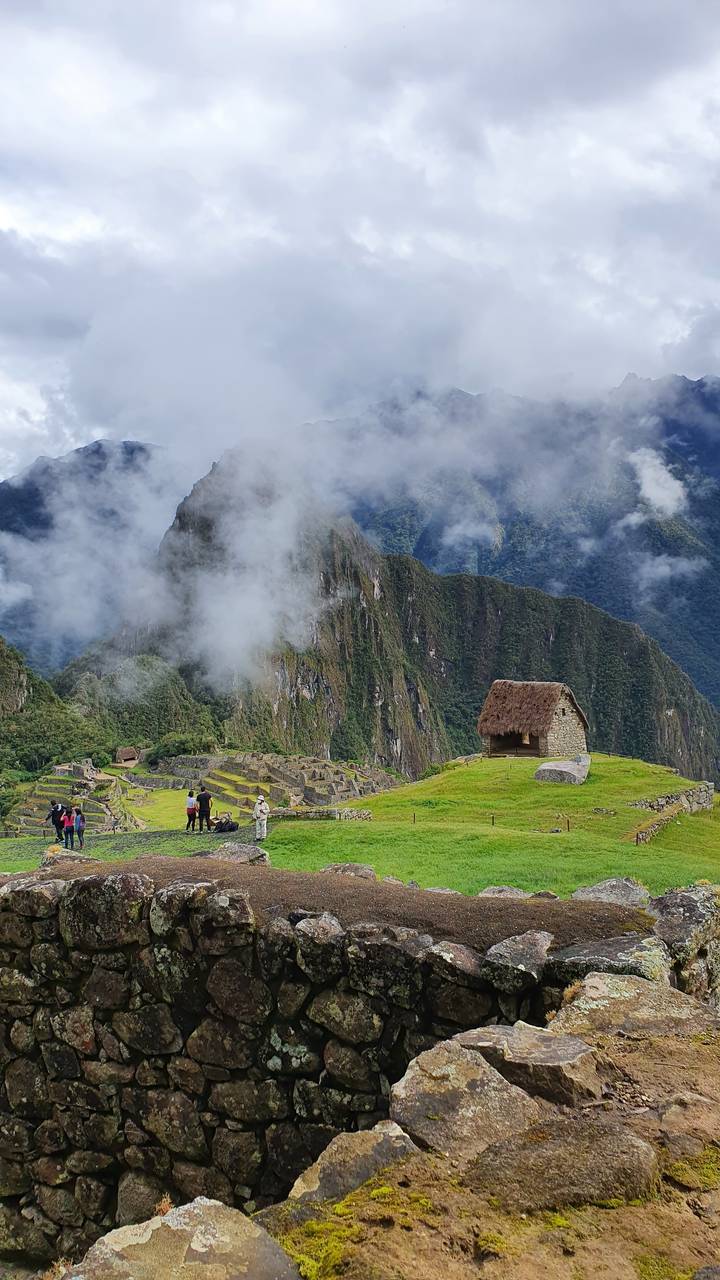 Tourists exploring ruins with mountains and clouds in the background.