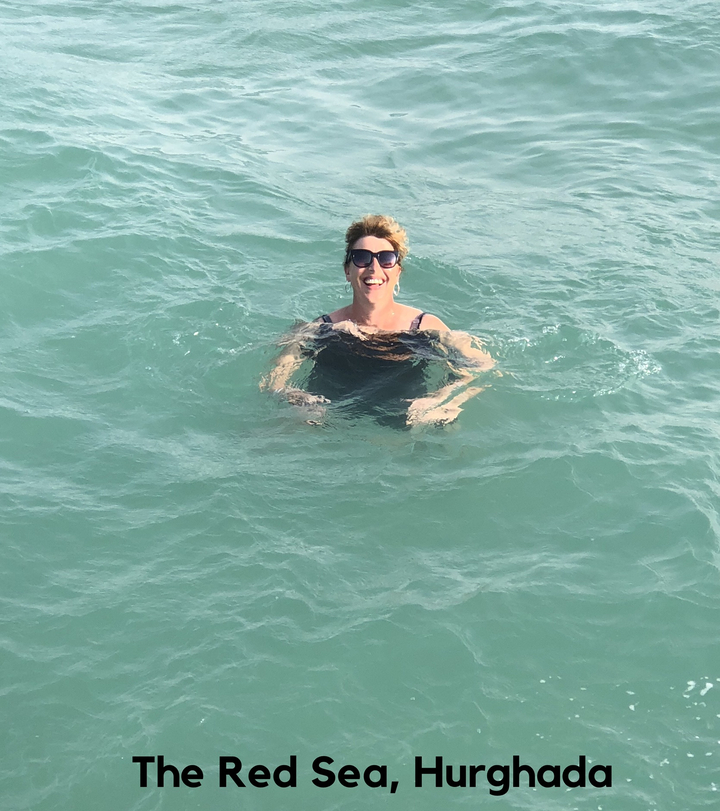 A person swimming in clear water, smiling at the camera.