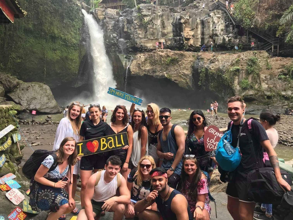 Group of people posing with signs in front of a waterfall.