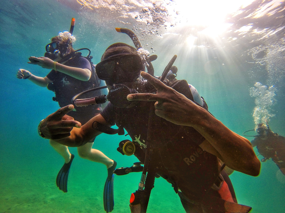 Scuba divers underwater with sunlight shining through the water.