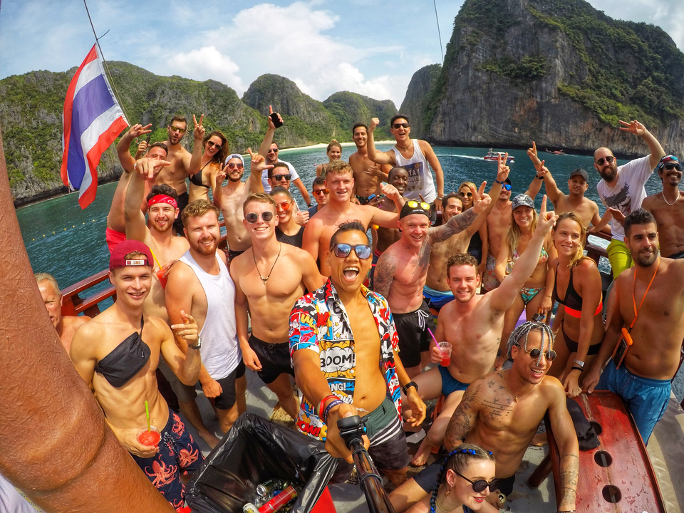 A group of friends posing happily on a beach with lush green cliffs in the background.