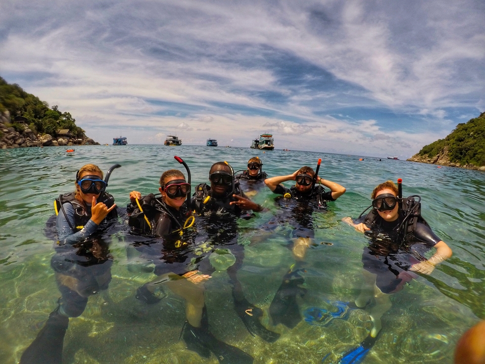Divers posing together in clear blue water with a scenic ocean view.