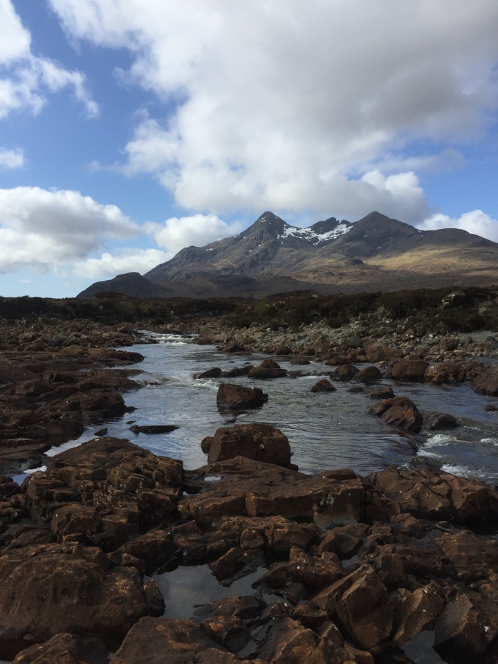 A rugged mountain range with a clear river flowing in the foreground.