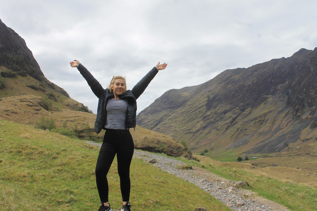 A person raising arms in celebration against a backdrop of rolling hills.