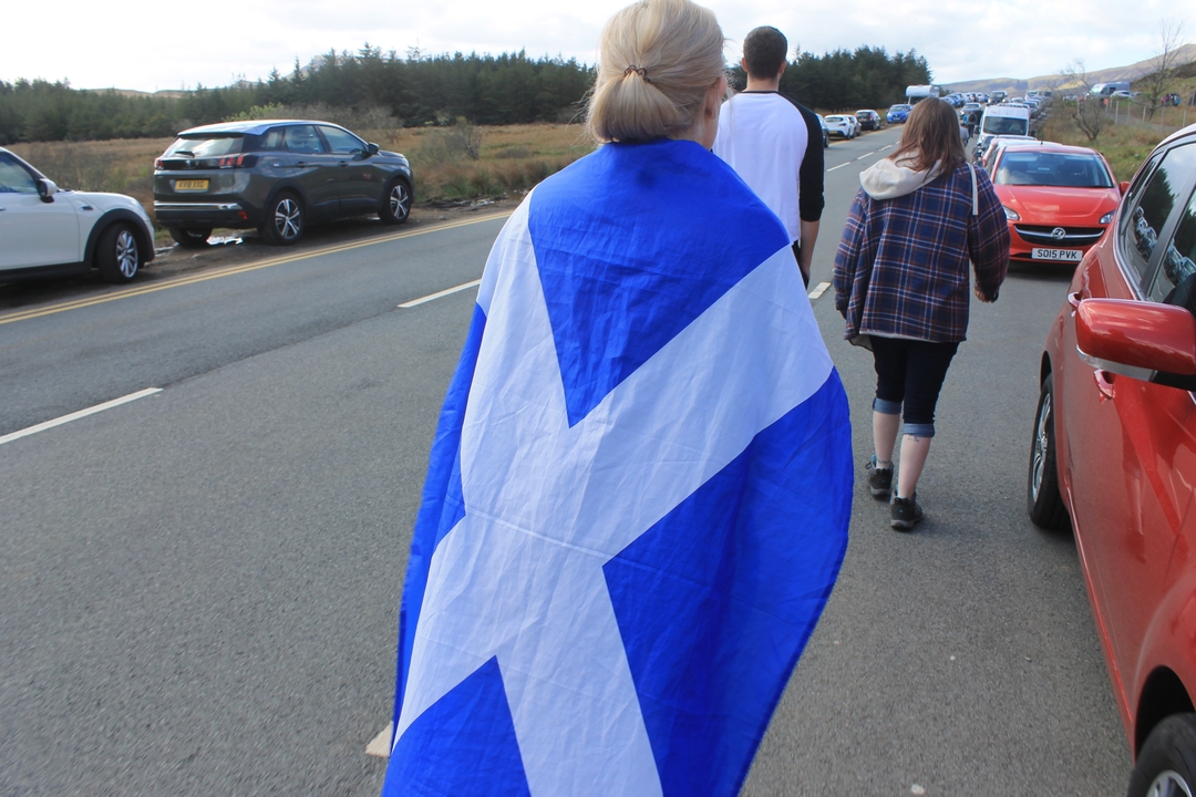 A person draped in a Scottish flag walking along a road.