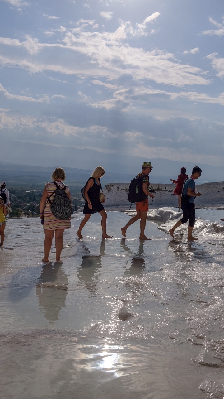 Tourists walking barefoot in shallow water at a natural site.