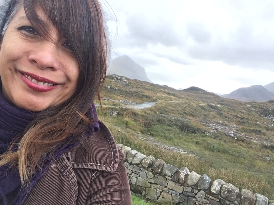 Personne posant en extérieur avec un paysage de montagne en arrière-plan.