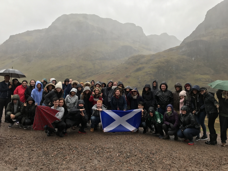 Group photo in front of scenic mountains with a Scottish flag.