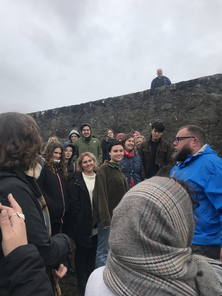 Groupe de personnes rassemblées près d'un mur de pierre en tenue décontractée.