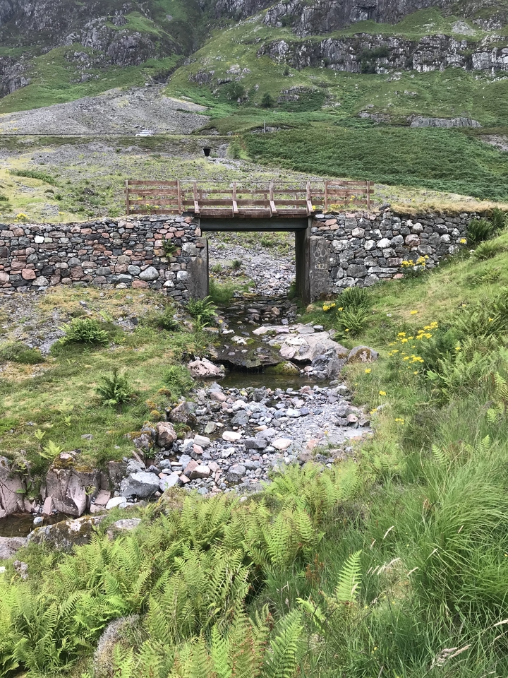 A small stone bridge over a shallow creek in a forested area.