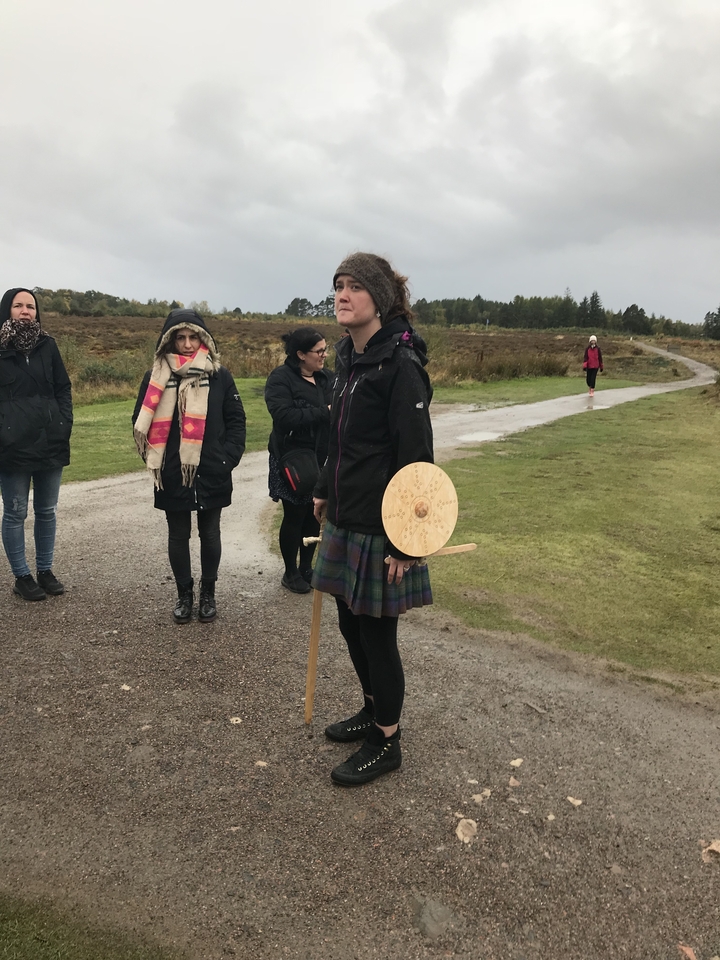 A person wearing a kilt and holding a shield, standing with a group.