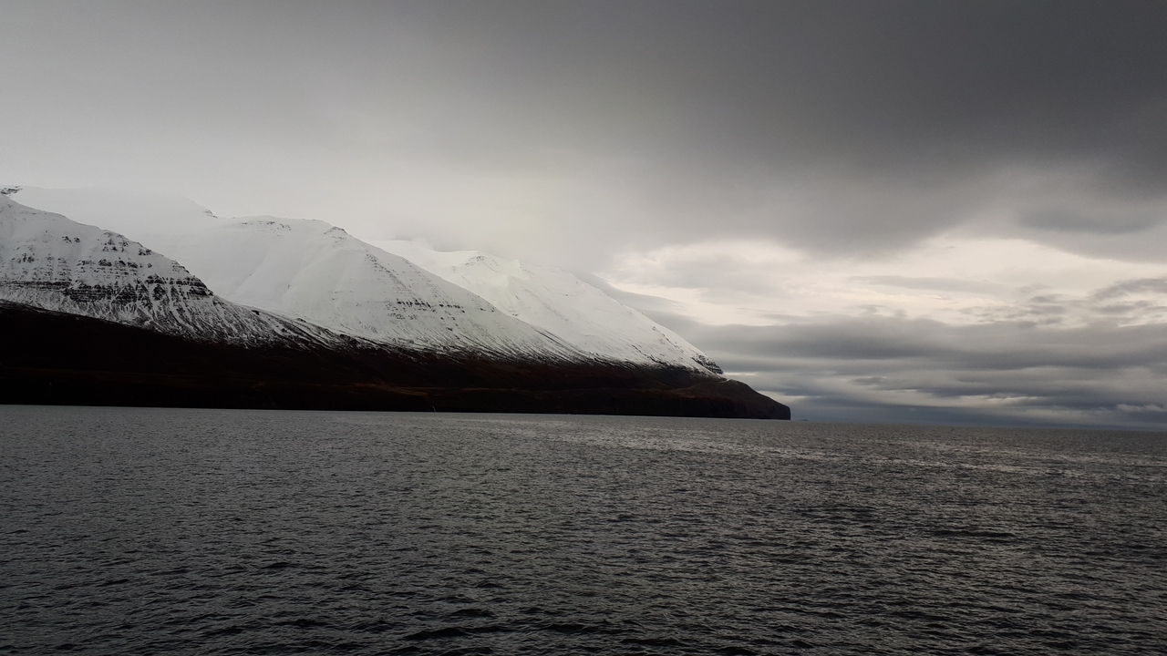 A view of a calm sea with mountains under a cloudy sky.