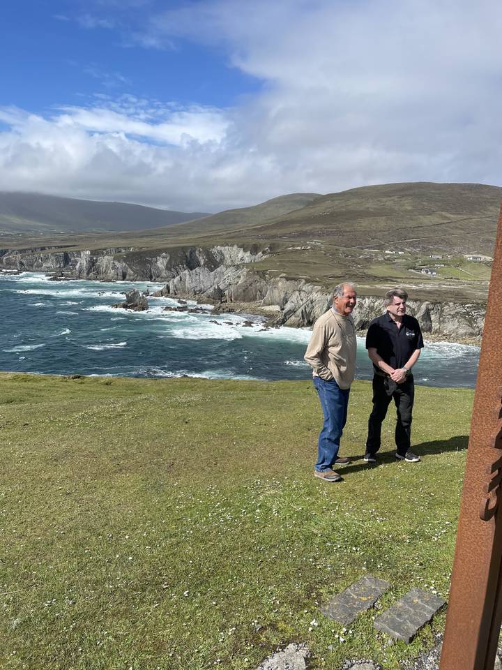 Two people standing on a grassy cliff with ocean waves below.