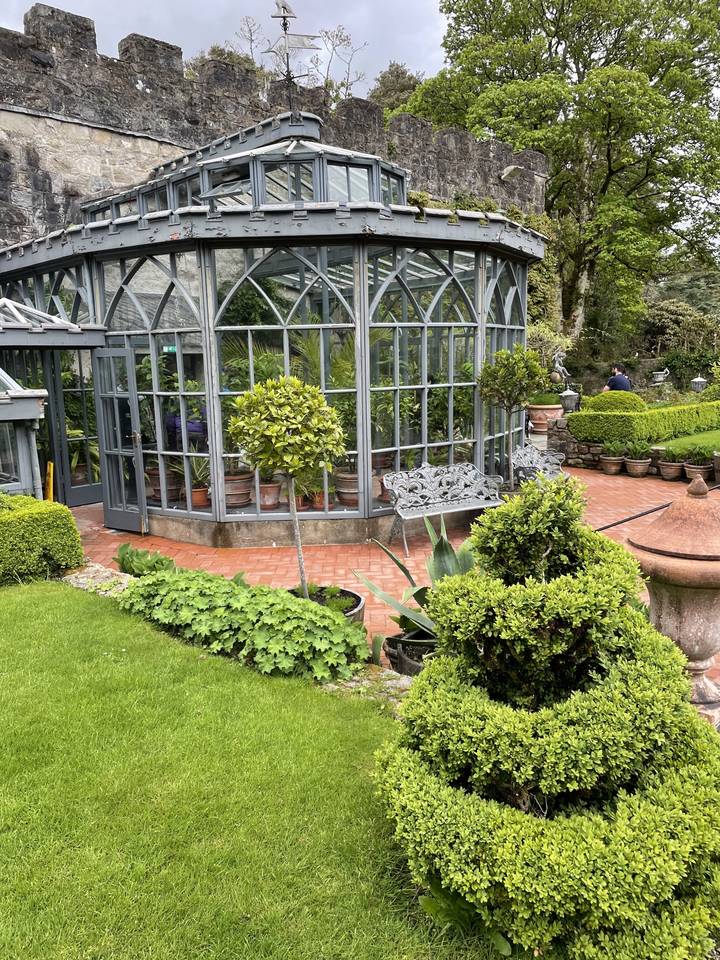 A glass conservatory with plants inside surrounded by brick patio.