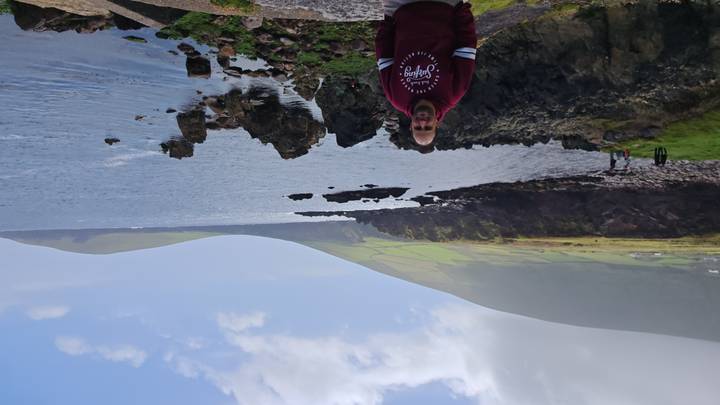 A person standing on the coast with cliffs in the background.