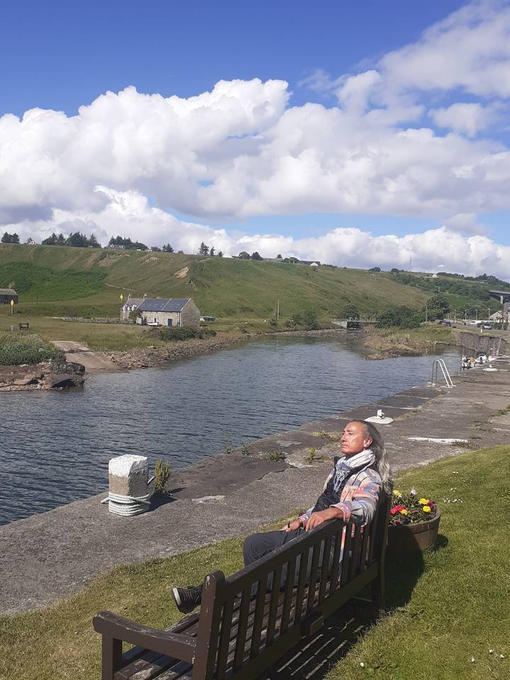 A person sitting by a waterway with buildings and boats.