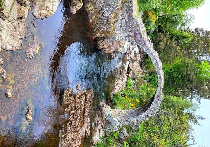 A scenic river flowing under an old stone bridge.