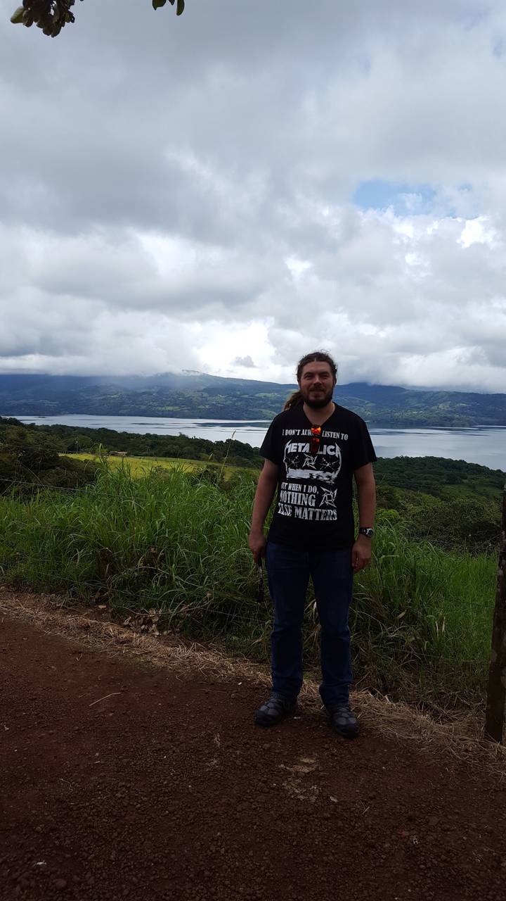 A man standing in front of a scenic landscape with a lake and mountains.