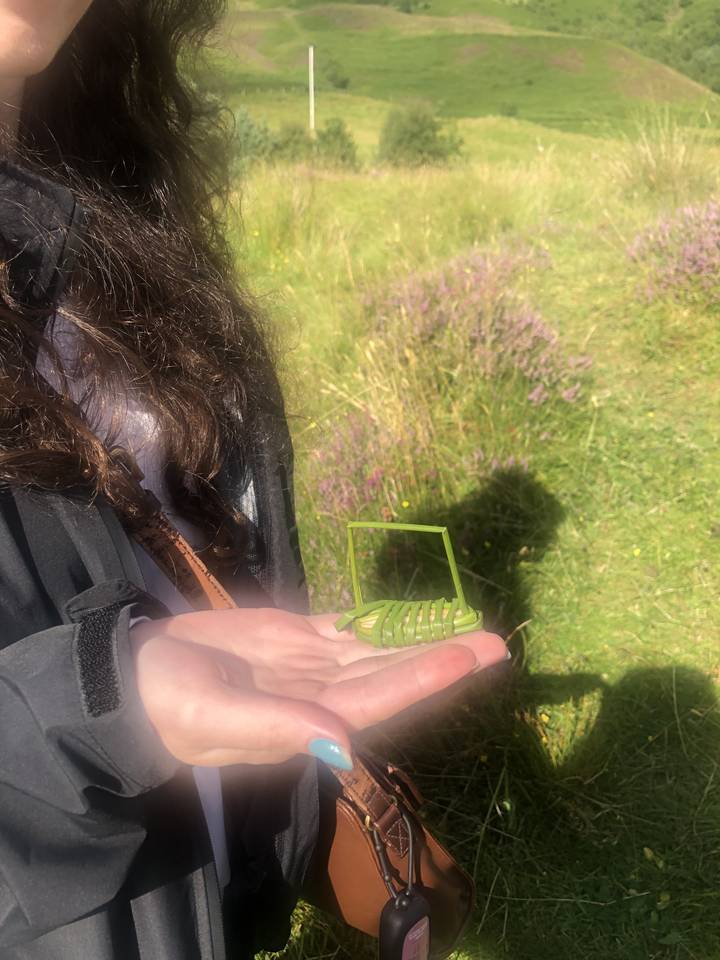 Person holding a small green object in an outdoor area.