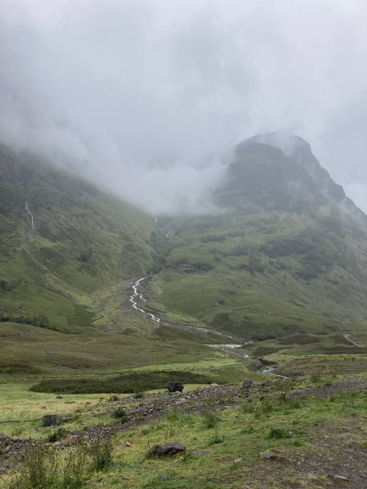 Pente de montagne verte escarpée enveloppée de brume avec un terrain rocheux.