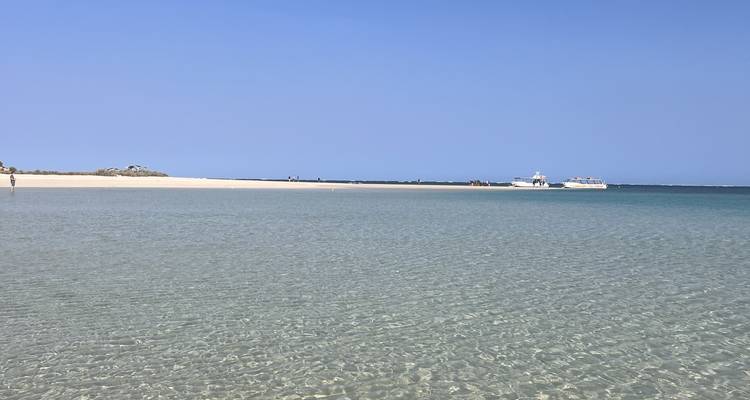 Shallow clear turquoise water with boats in the distance.