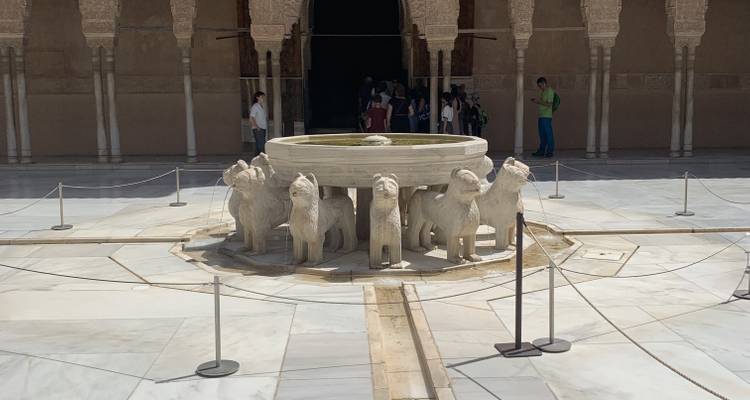 Fuente de piedra ornamentada rodeada de arcos con visitantes.