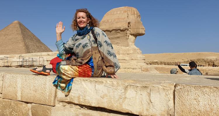 Femme assise près du Sphinx et des pyramides qui pose.