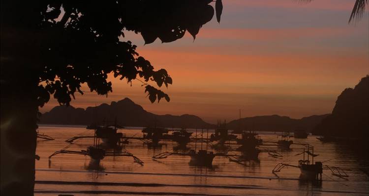 Silhouette de bateaux sur une étendue d'eau calme avec un coucher de soleil coloré.