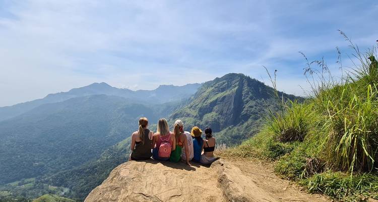 People sitting on a rock ledge with a scenic mountain view.