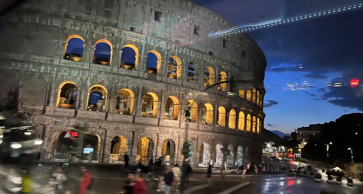 The Colosseum illuminated at night with people around.